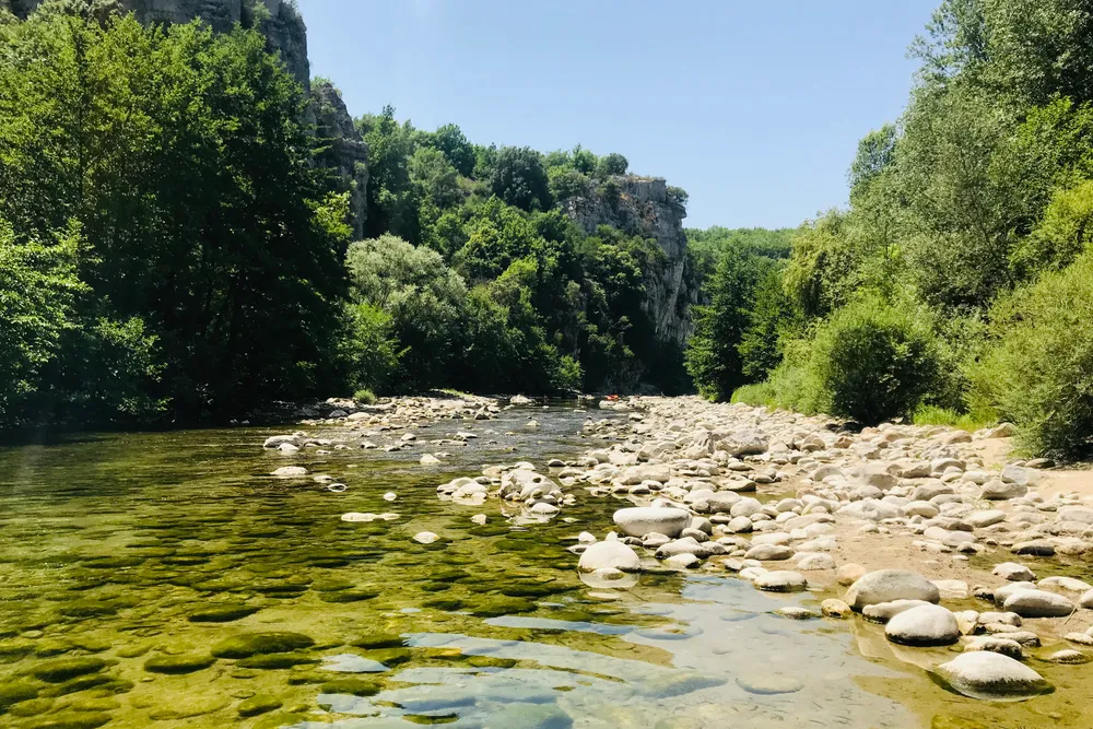 Klares Wasser über hellen Kieseln, eingerahmt von bewaldeten Felshängen